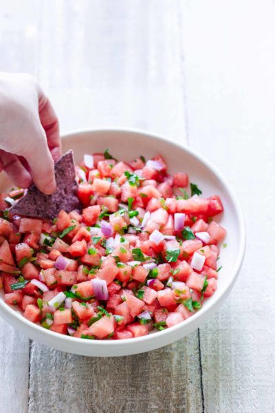 Watermelon salsa in bowl with hand dipping a corn chip