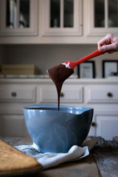 Melted chocolate dripping from a spatula into a bowl, an ingredient in my yellow cake