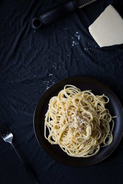 Cacio e pepe on a plate, surrounded by a form and a block of parmesan cheese