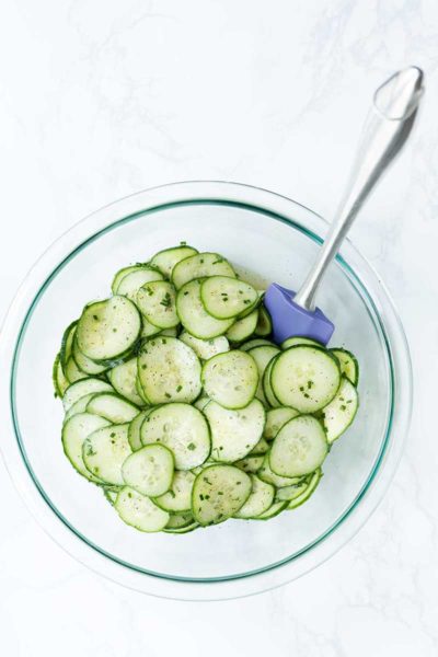 Close up shot of cucumber salad in a large bowl with a spatula.