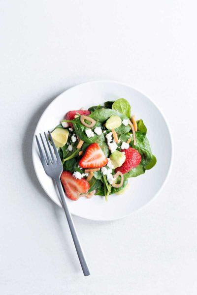 Overhead photo of a strawberry spinach salad recipe on a white plate with a silver fork.