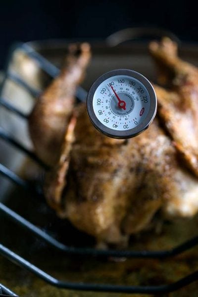 A roasting pan with a whole roasted chicken and a thermometer - showing incorrect chicken internal temperature