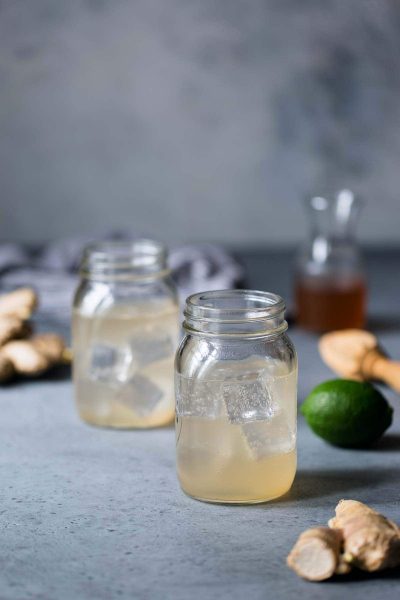 Two mason jars filled with homemade ginger ale, surrounded by homemade ginger syrup, limes and fresh ginger