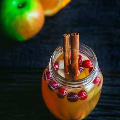 overhead image of fall sangria in mason jar glass with cinnamon sticks and fresh cranberries
