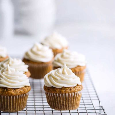 baked cupcakes topped with cream cheese frosting on a cooling rack