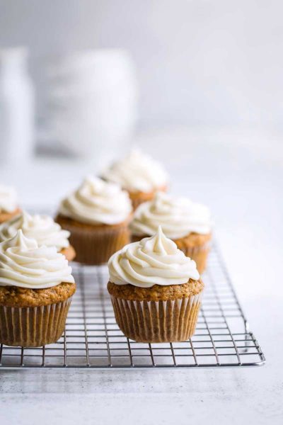 baked cupcakes topped with cream cheese frosting on a cooling rack