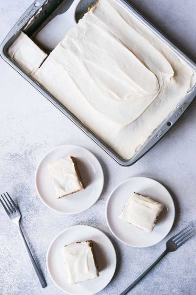 Pumpkin cake with cream cheese frosting in a pan, with three slices on plates.