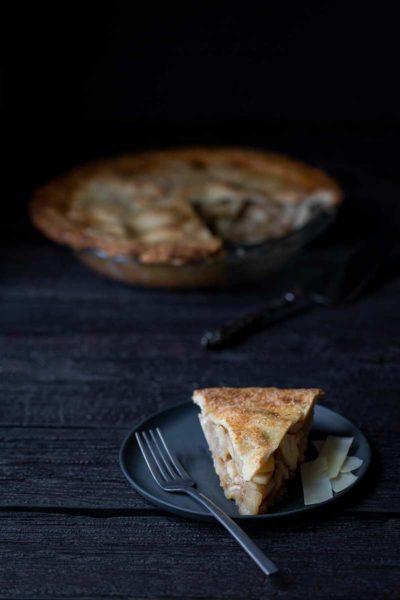 A slice of Classic Homemade Apple Pie on a plate, with the full apple pie recipe in the background