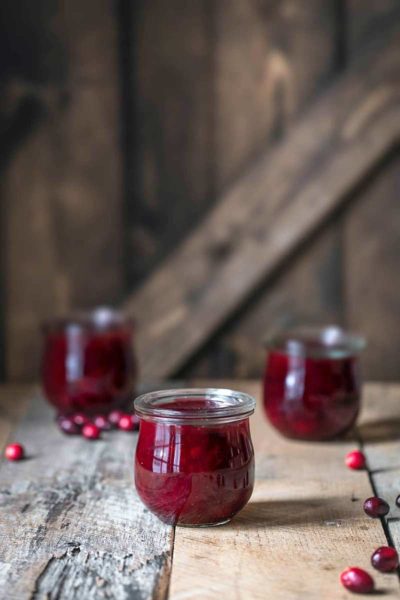 Homemade Cranberry Sauce Recipe in three mason jars, surrounded by scattered cranberries.