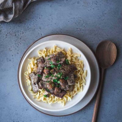 overhead photo: plate with classic beef stroganoff over buttered noodles. Wooden spoon next to plate