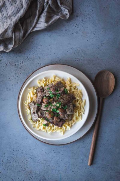 overhead photo: plate with classic beef stroganoff over buttered noodles. Wooden spoon next to plate