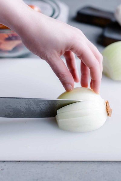 How To Chop An Onion Tutorial showing a hand pressing an onion halve onto a cutting board while a knife makes a slice