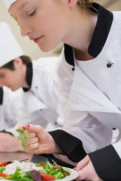 female culinary school student adding fresh herbs to a plated dish