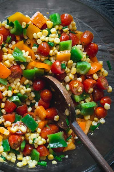 Corn salad in a grey bowl surrounded by bell peppers and tomatoes