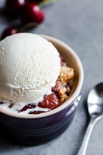 Cherry crisp in a small bowl topped with a scoop of vanilla ice cream