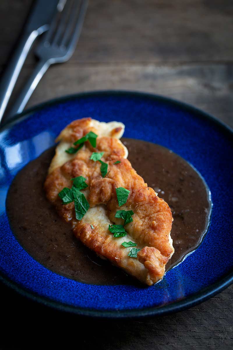 A photo of pan-seared chicken breast topped with a pan sauce recipe and fresh chopped parsley