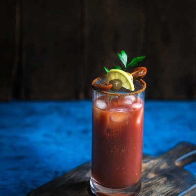 Old Bay Bloody Mary topped with garnishes on a blue backdrop