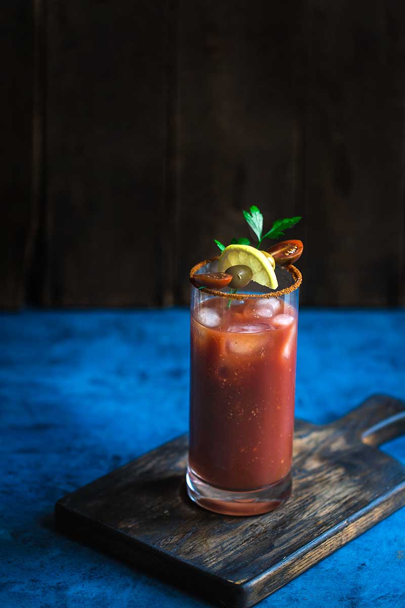 Old Bay Bloody Mary topped with garnishes on a blue backdrop
