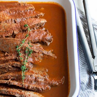 Braised beef brisket in a rectangular serving dish, with kitchen tongs on the right