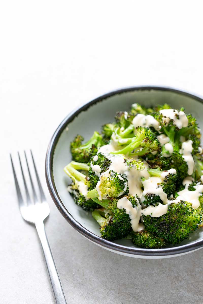 bowl of broccoli with cheese sauce next to a fork