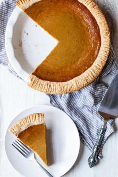 Overhead photo of pumpkin pie from scratch in a pie dish next to a slice of pumpkin pie