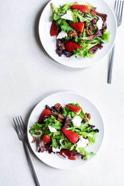 Mixed greens salad with strawberries, pecans and feta on a plate with a fork.