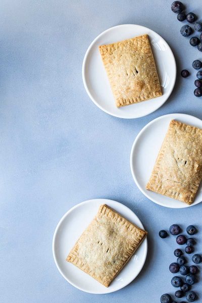 Three blueberry pop tarts on plates, surrounded by blueberries